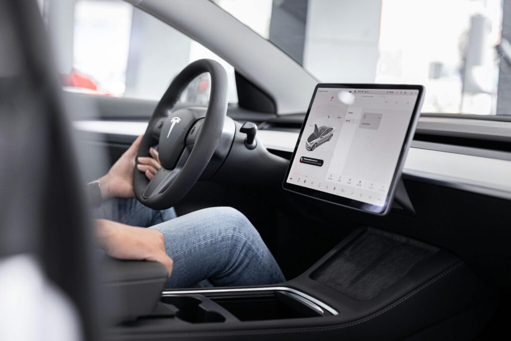 Interior of an electric car showing steering wheel and large touchscreen display, indicating modern technology.